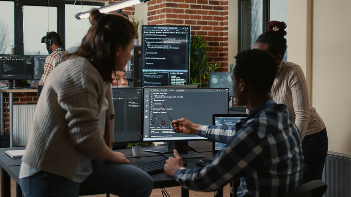 Team of three people discussing cybersecurity objectives looking at multiple computer screens
